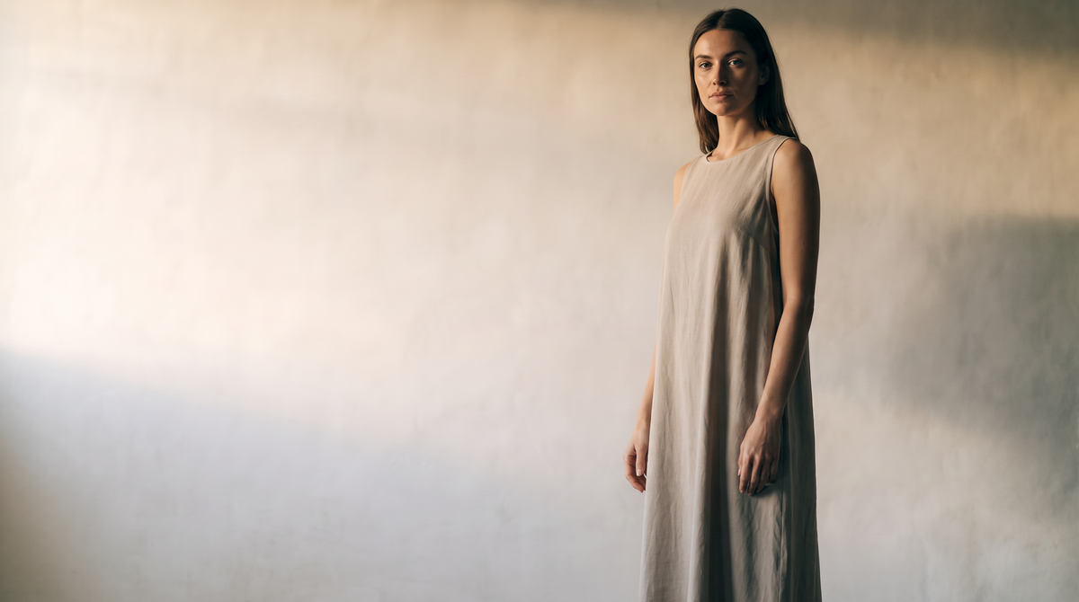 Woman in a flowing stone-colored midi dress against a warm plaster wall in morning light — Kessoro